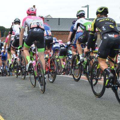A group of competitive cyclists in colourful jerseys riding closely together on a road, captured from behind.