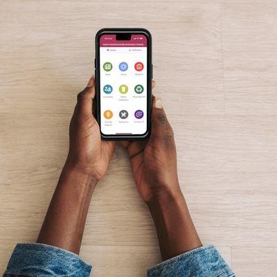 Hands holding a smartphone displaying a health and wellness app with colourful icons on a light wooden surface.